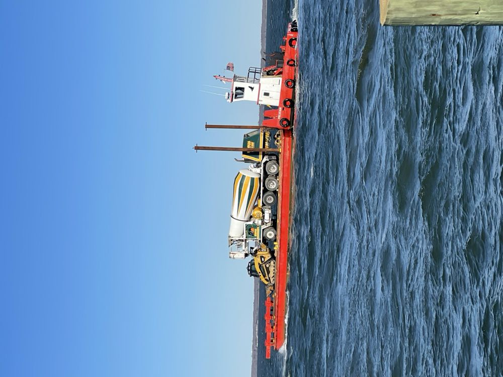 A Nicolia mixer truck being moved by barge across the water