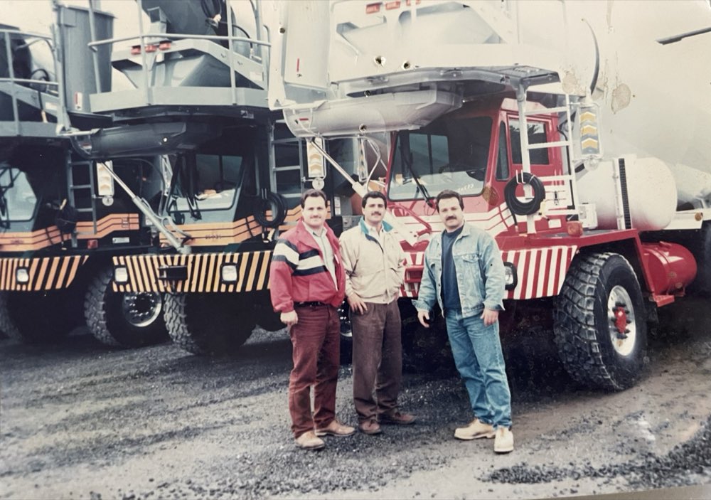 Three men standing beside a Nicolia front-discharge mixer, from the family archive
